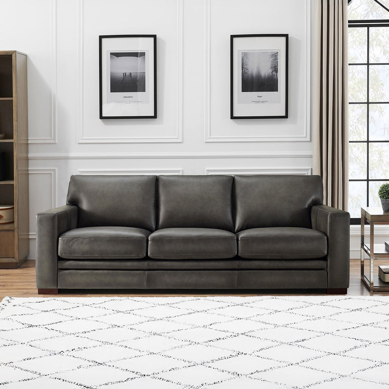 Gray sofa in a living room with a bookshelf, rug, and window.